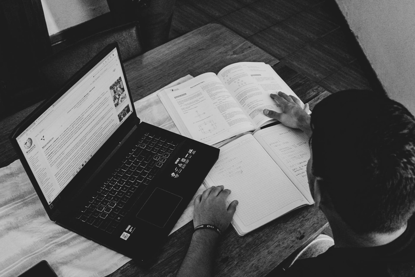 Studente che studia a una scrivania di legno con un laptop e un libro di testo.